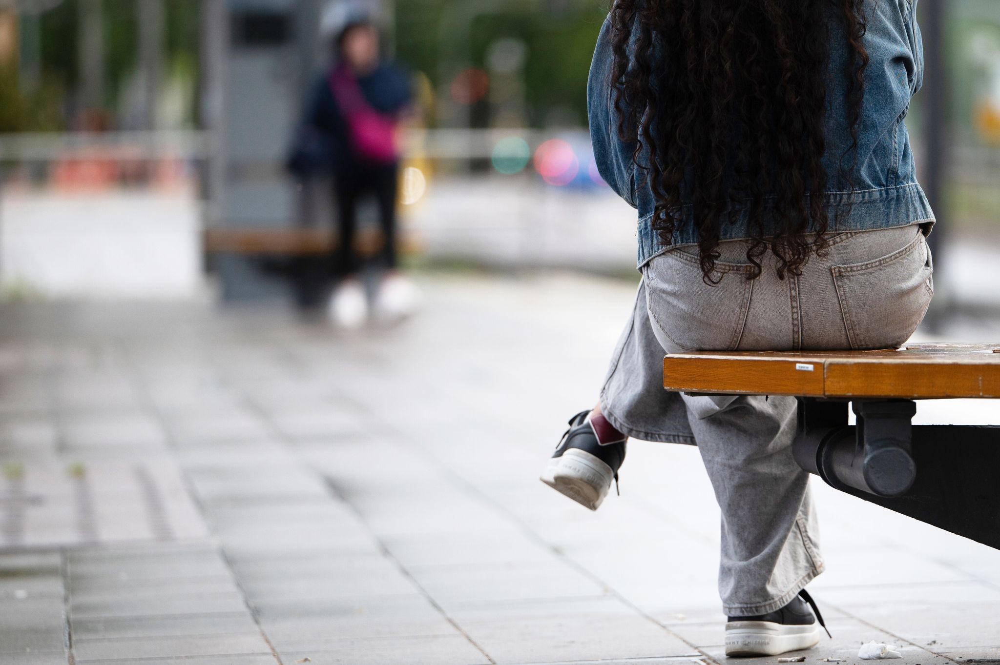 Eine junge Frau sitzt an einer Haltestelle auf einer Bank