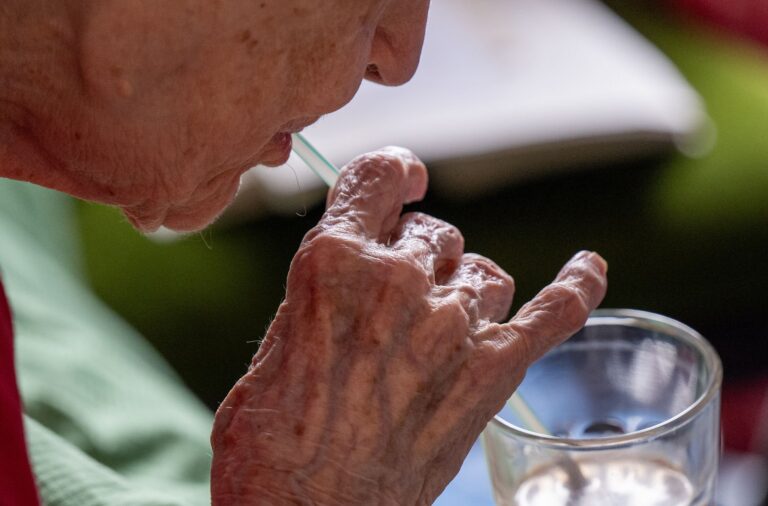 Eine Seniorin trinkt mithilfe eines Strohhalms