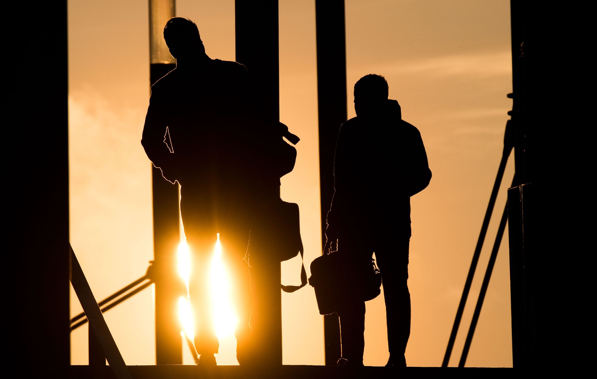 Zwei Männer gehen mit Aktentasche bei Sonnenaufgang über Brücke